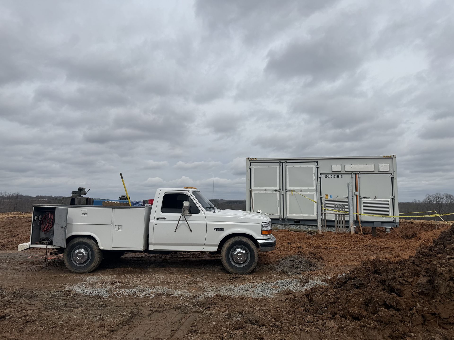 White pickup truck parked near a modular building on a construction site under a cloudy sky.