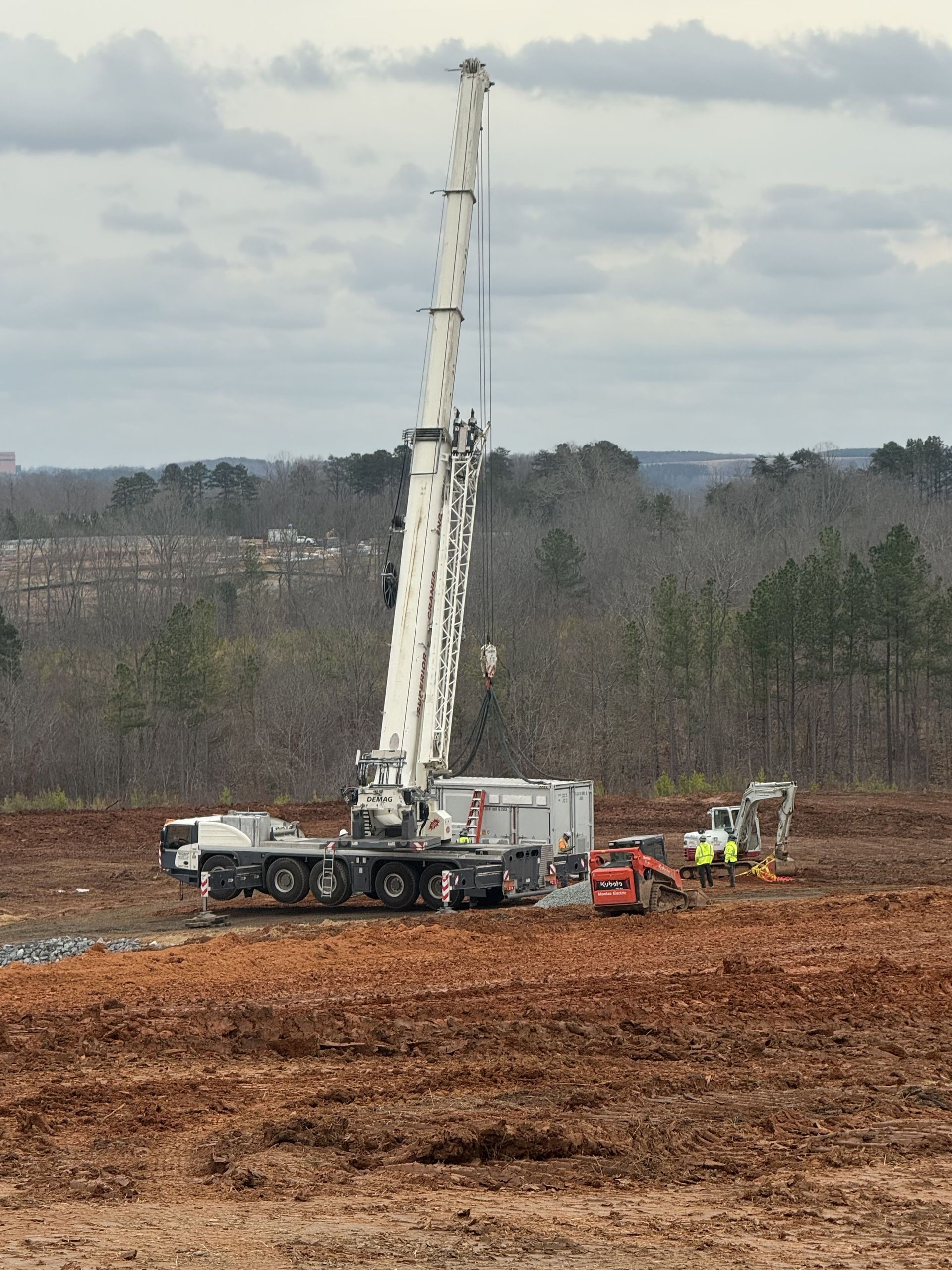 Large white drilling rig in a brown field, with other construction equipment and a cloudy sky.