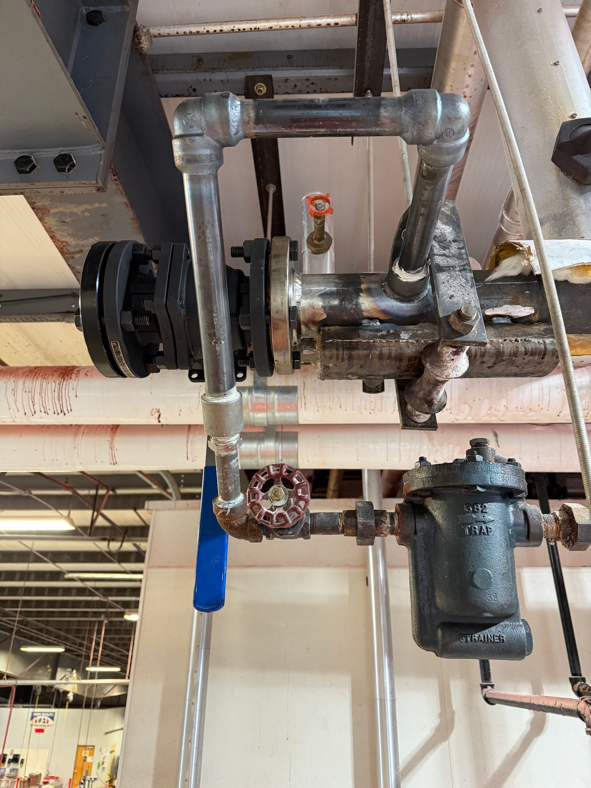 Industrial piping system with valves, flanges, and a steam trap.