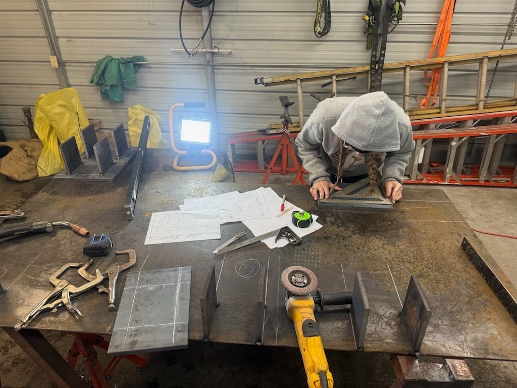 Person on a ladder working inside a garage with equipment including a welding torch and oxygen tank.