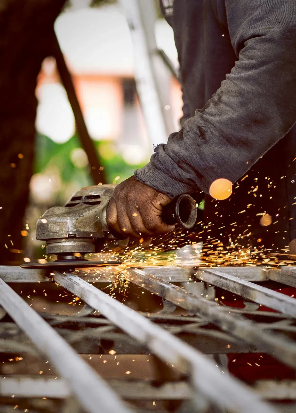 Person using an angle grinder, creating sparks, on metal bars, outdoors.