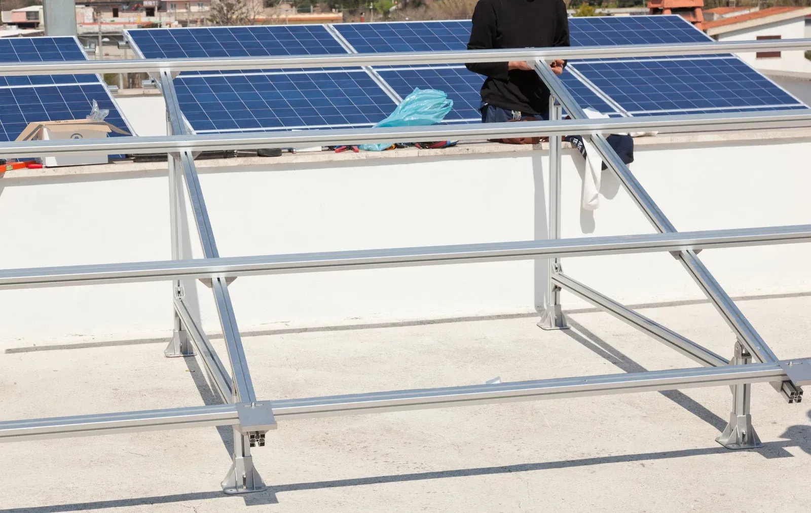 Solar panel installation on a rooftop: worker on a metal frame, panels installed, blue sky.