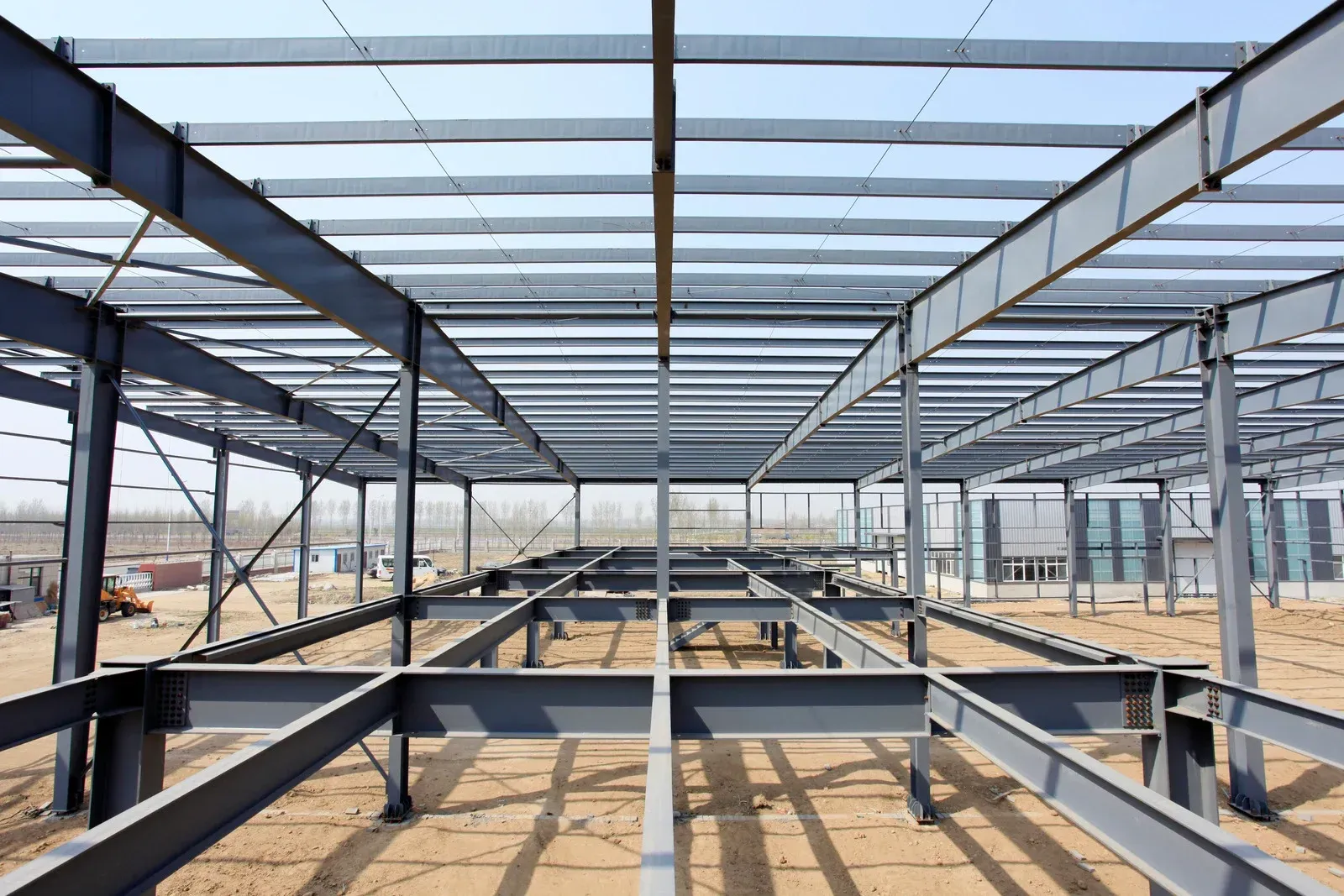 Steel framework of a large building under construction against a blue sky.