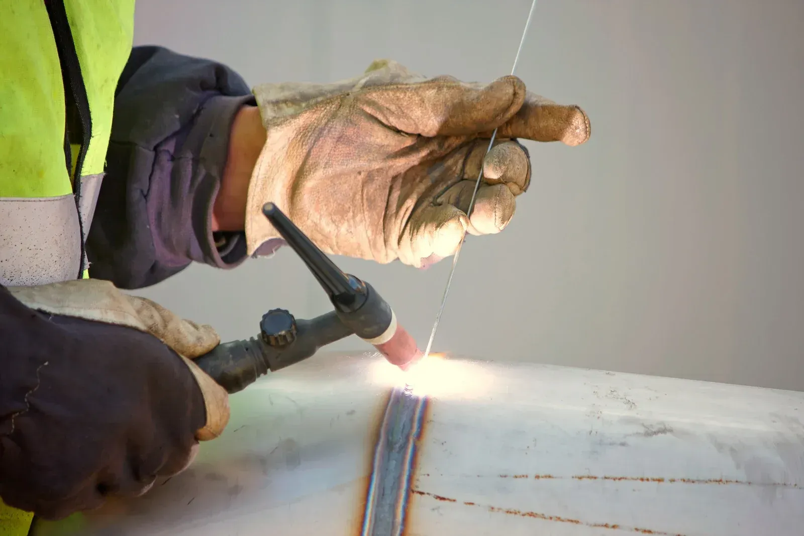 Welder using a torch on a metal pipe, wearing gloves and safety gear, creating a weld.