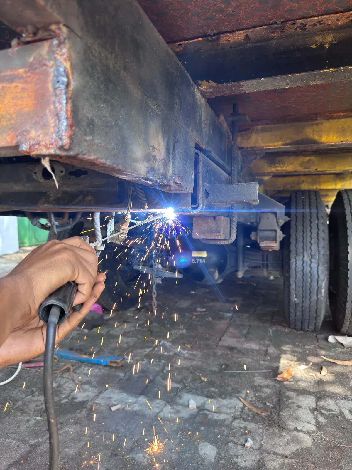 Welder wearing gloves and red long sleeve welding metal, sparks flying.