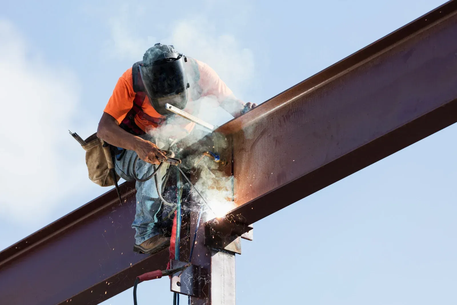Person using an angle grinder, creating sparks, on metal bars, outdoors.