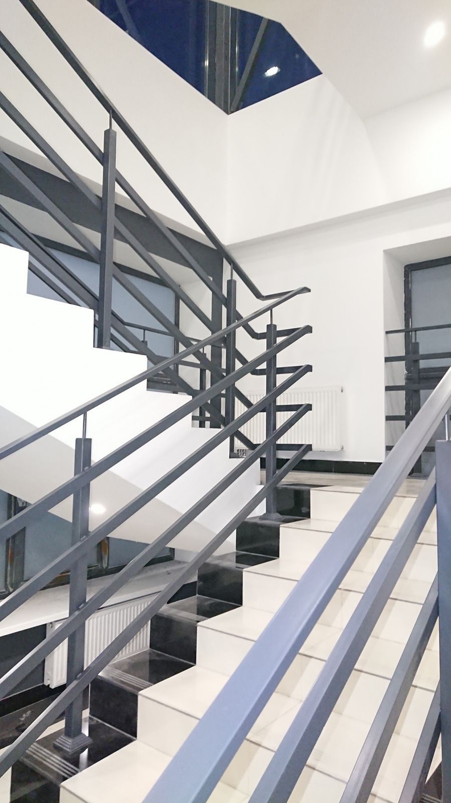 Staircase with gray metal railings, white walls, and black steps.