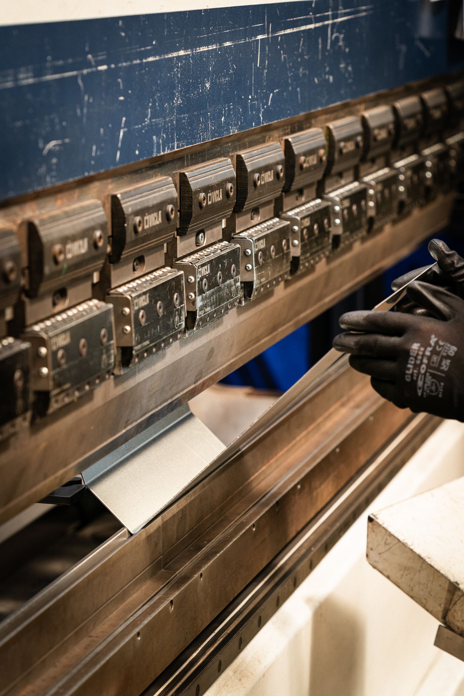 Lamiera piegata da una pressa idraulica, si vedono le mani guantate della persona.