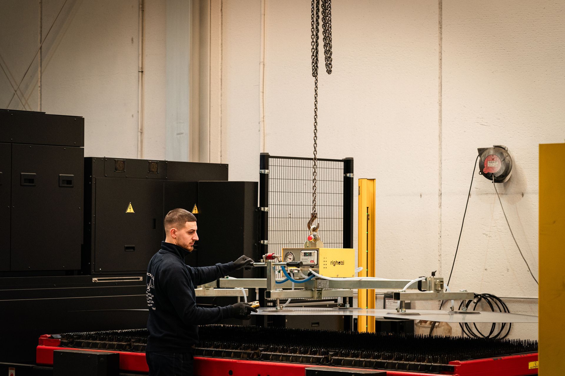 Uomo che aziona macchinari in una fabbrica. Una gru è sospesa sopra.