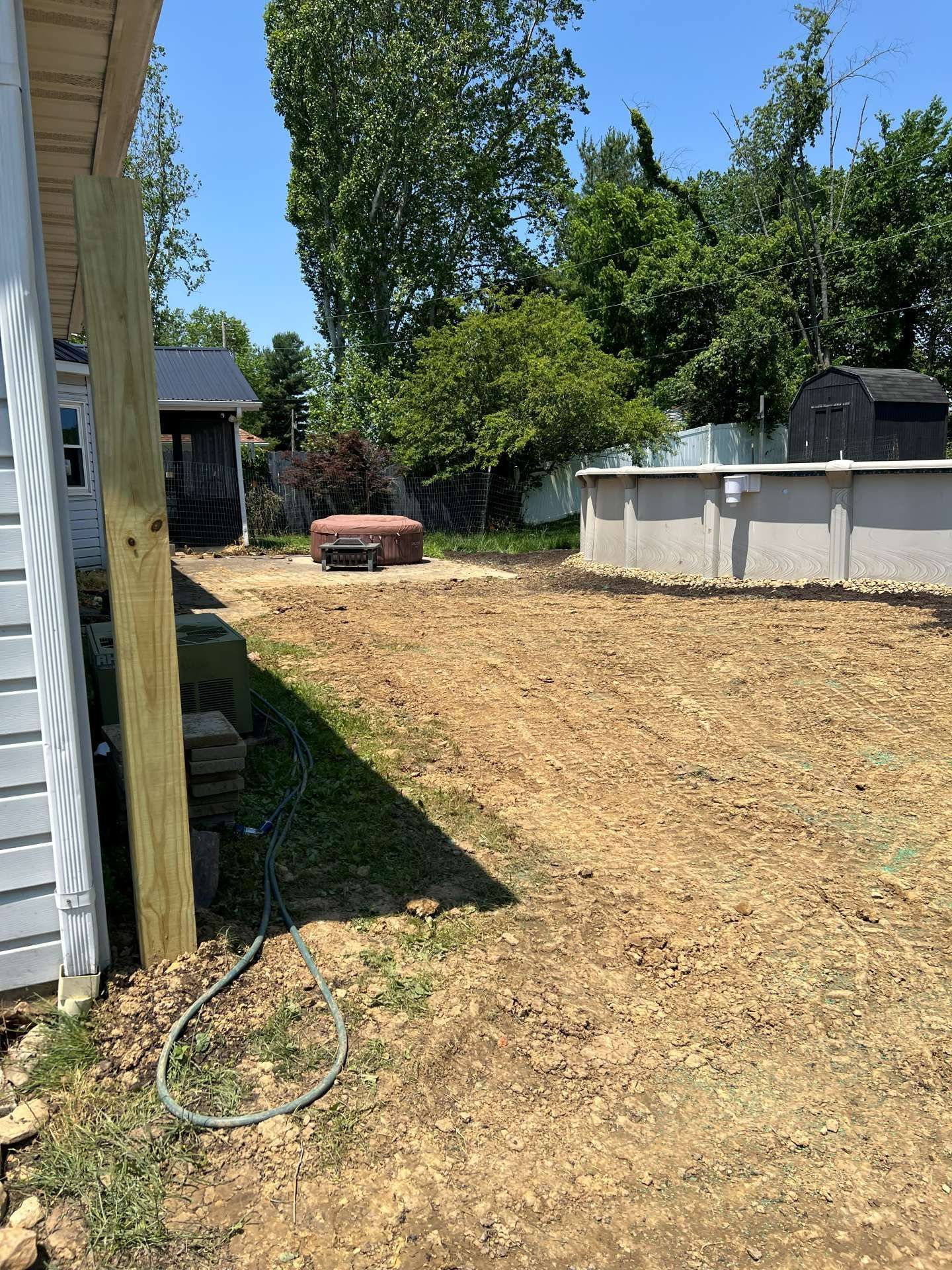 Backyard with dry grass, a white house wall, trees, and an above-ground pool in the background