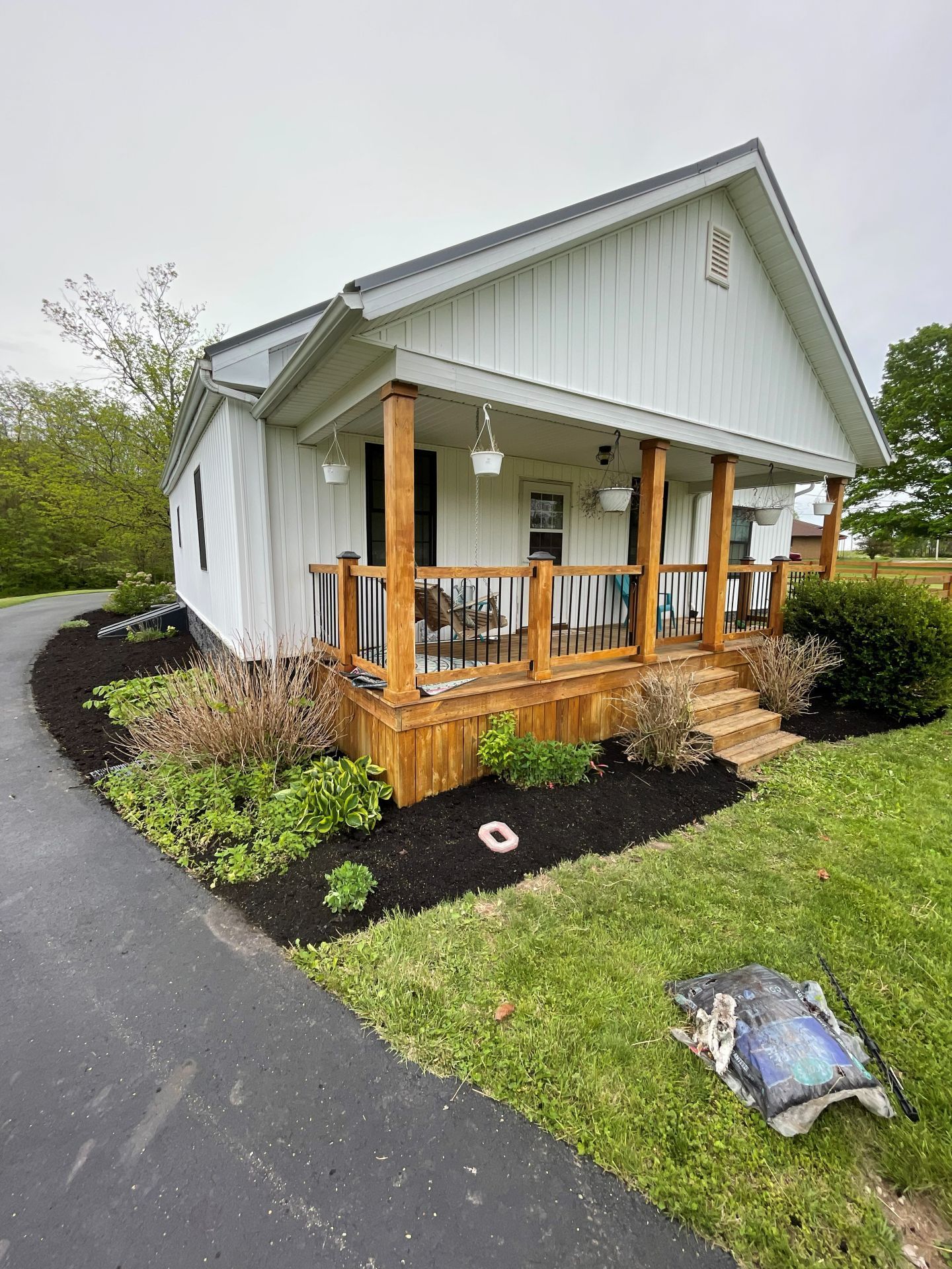 Small white house with wooden porch, curved driveway, and landscaped lawn on a cloudy day