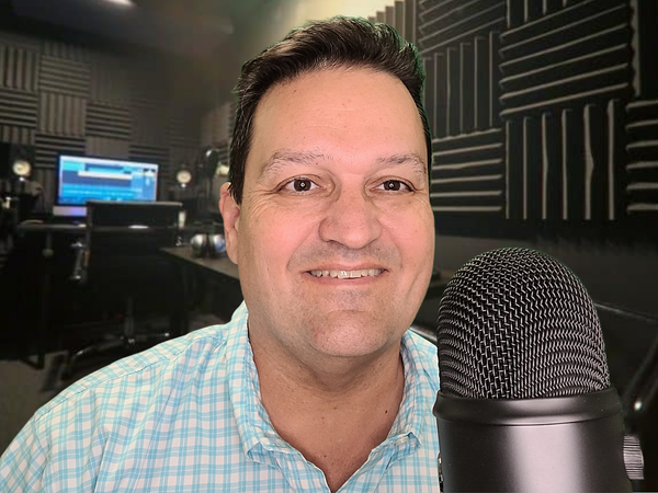 A man is smiling in front of a microphone in a recording studio.