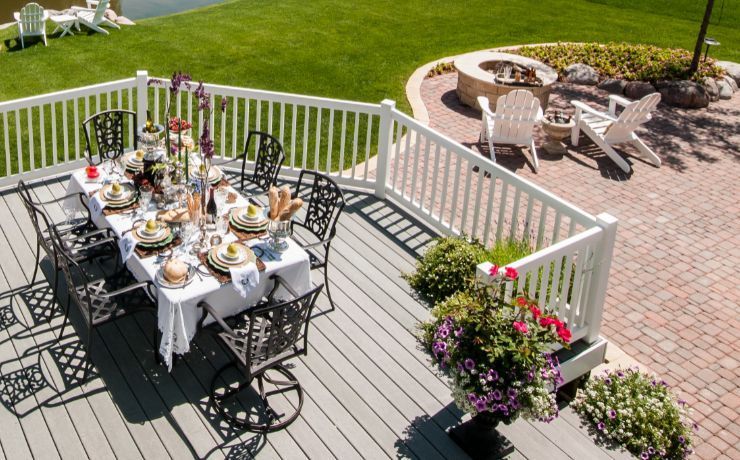 A photo of a patio that is built next to a deck in the backyard of a beautiful luxury home in Glendale, California The patio has a built-in firepit and chairs surrounding the firepit. The deck has a lot of flowers.