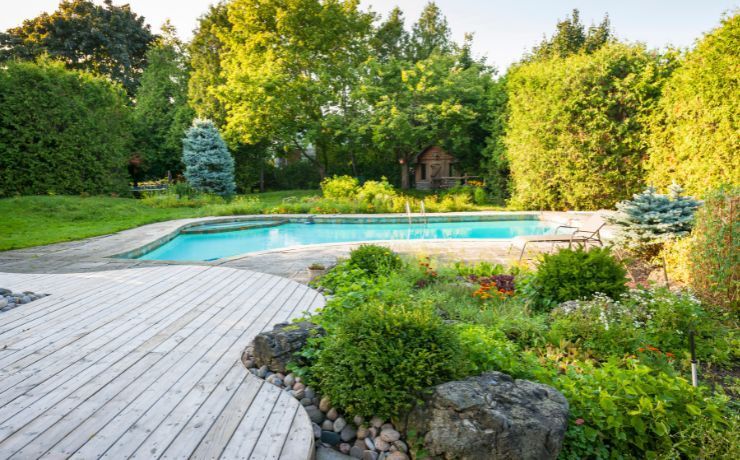 A photo of a deck that surrounds a pool. The backyard is enclosed with a wall of trees and does not need a fence.
