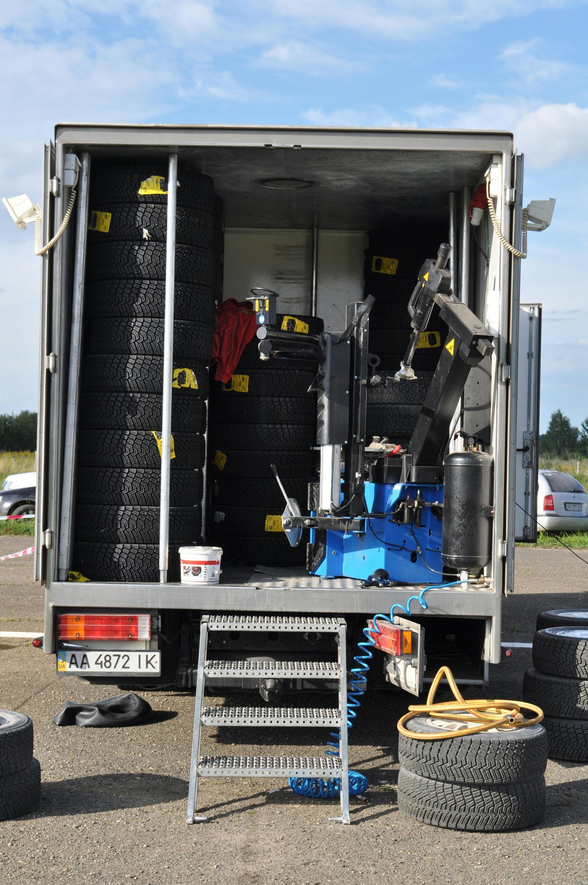 Truck interior with tires, tire changer, and tools, likely a mobile tire service at an outdoor event.