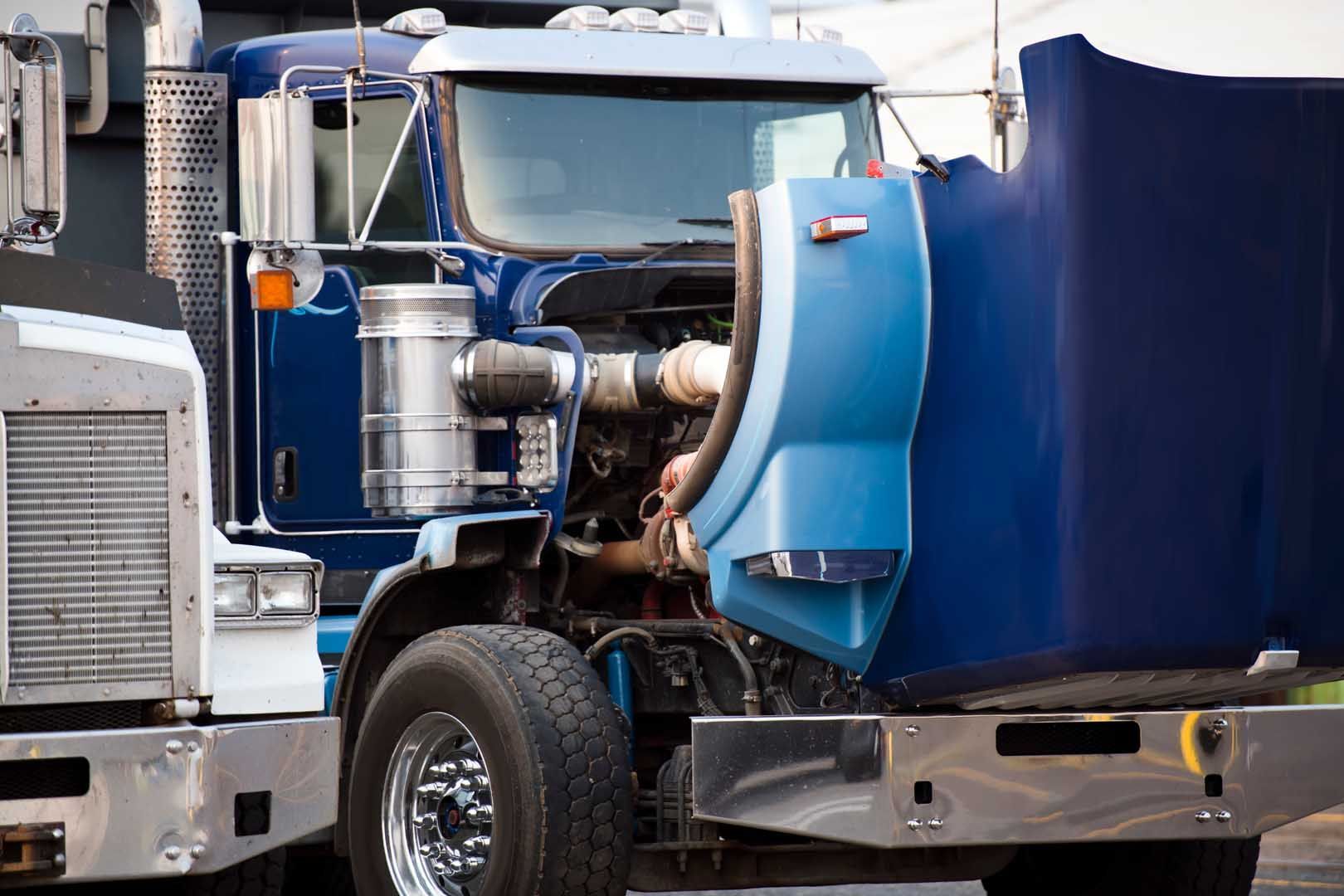 Blue semi-truck with hood open, revealing engine. Outdoors, daylight.