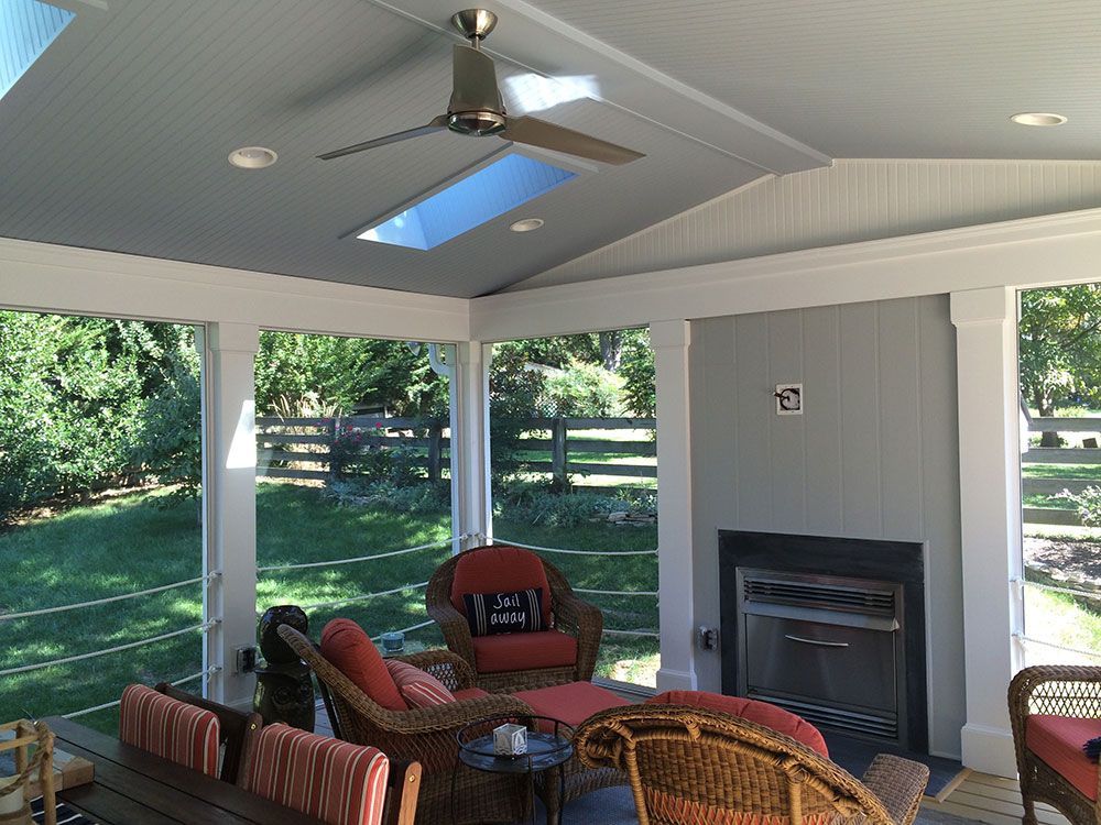 A screened in porch with a fireplace and a ceiling fan