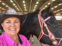 A woman in a cowboy hat is standing next to a black horse.