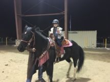 A young girl is riding on the back of a black horse.