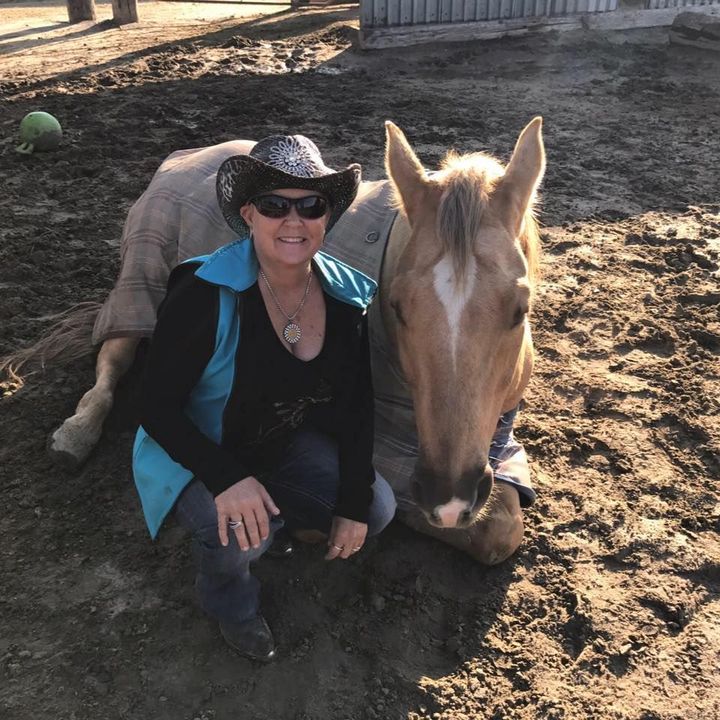 A woman in a cowboy hat is kneeling next to a horse