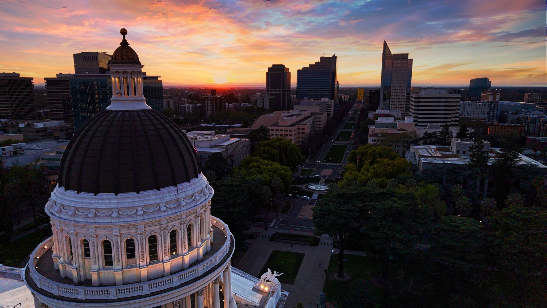Dome of a historic building at sunset with a city skyline and glowing orange sky in the background