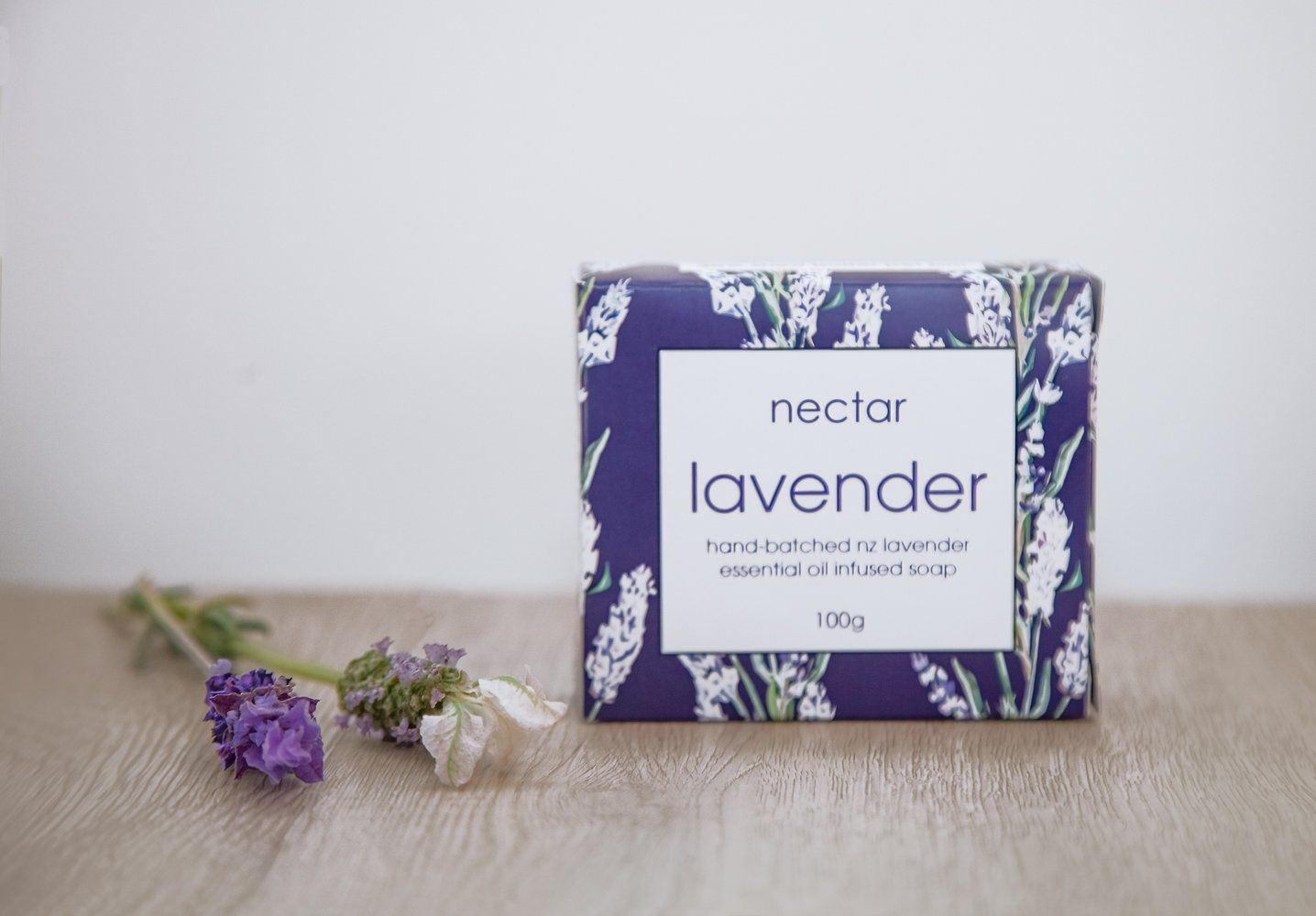 Bar of lavender soap with lavender sprig on a wooden surface. Purple and white packaging.