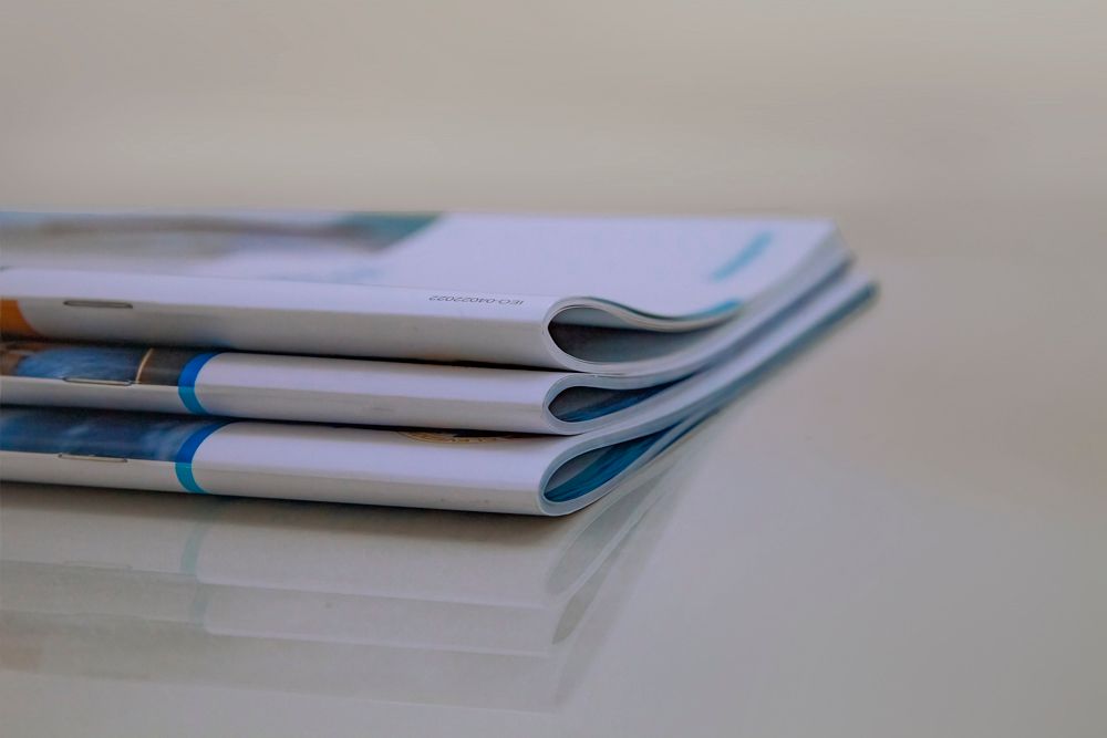 Stack of three brochures on a reflective surface. Blue and white covers with visible pages.