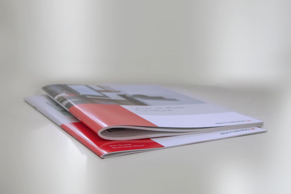 Two brochures stacked, with red and white covers, on a white surface. From Excel In Print Auckland. 