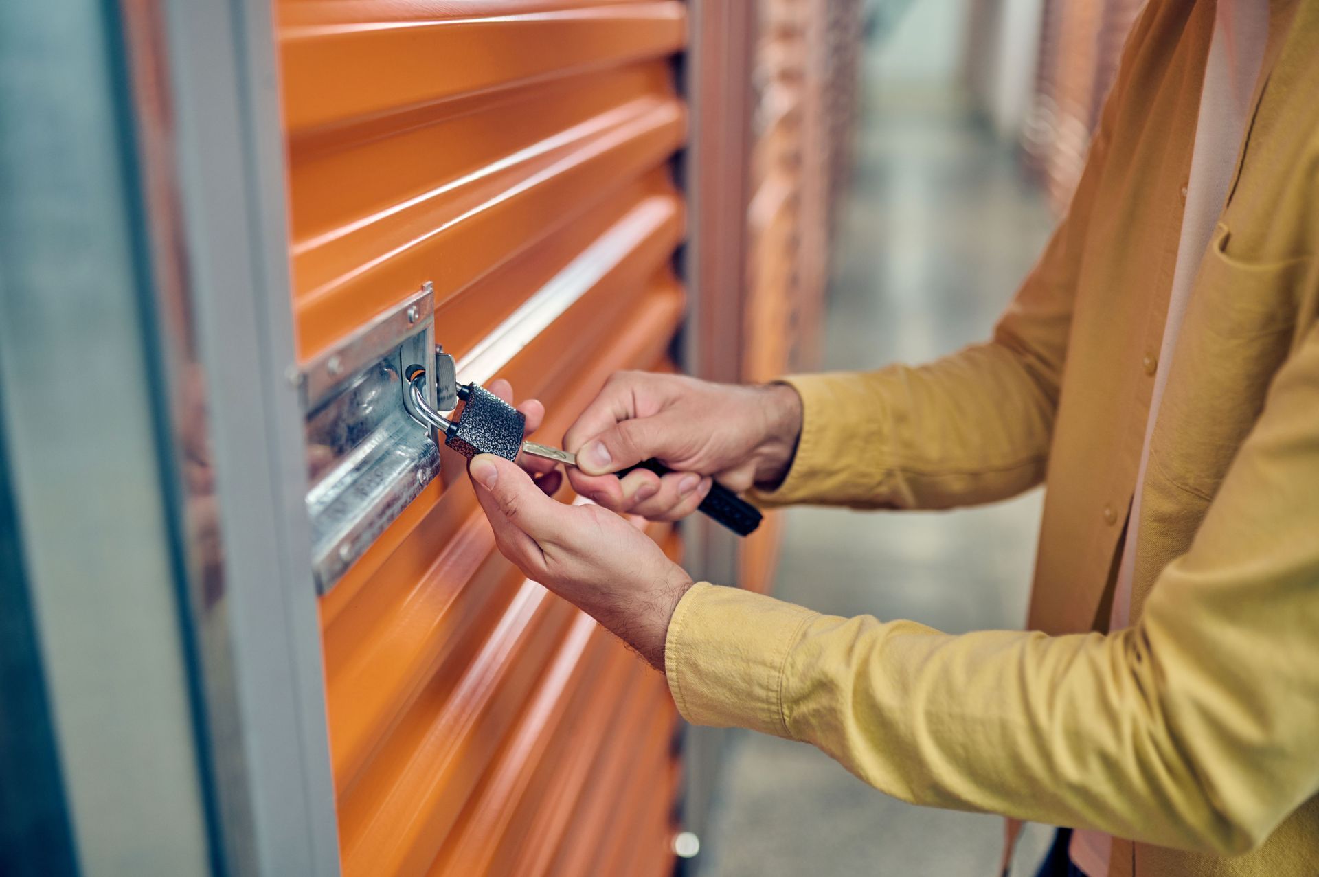 A worker unlocks a padlock placed on the orange door of a storage unit.