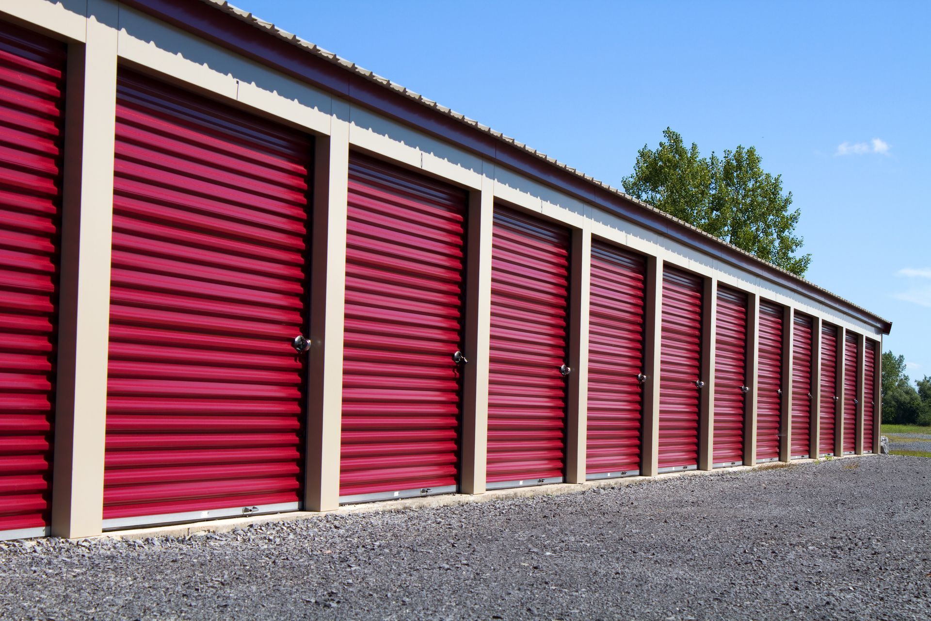 Row of red storage unit doors in a gravel lot under a clear blue sky
