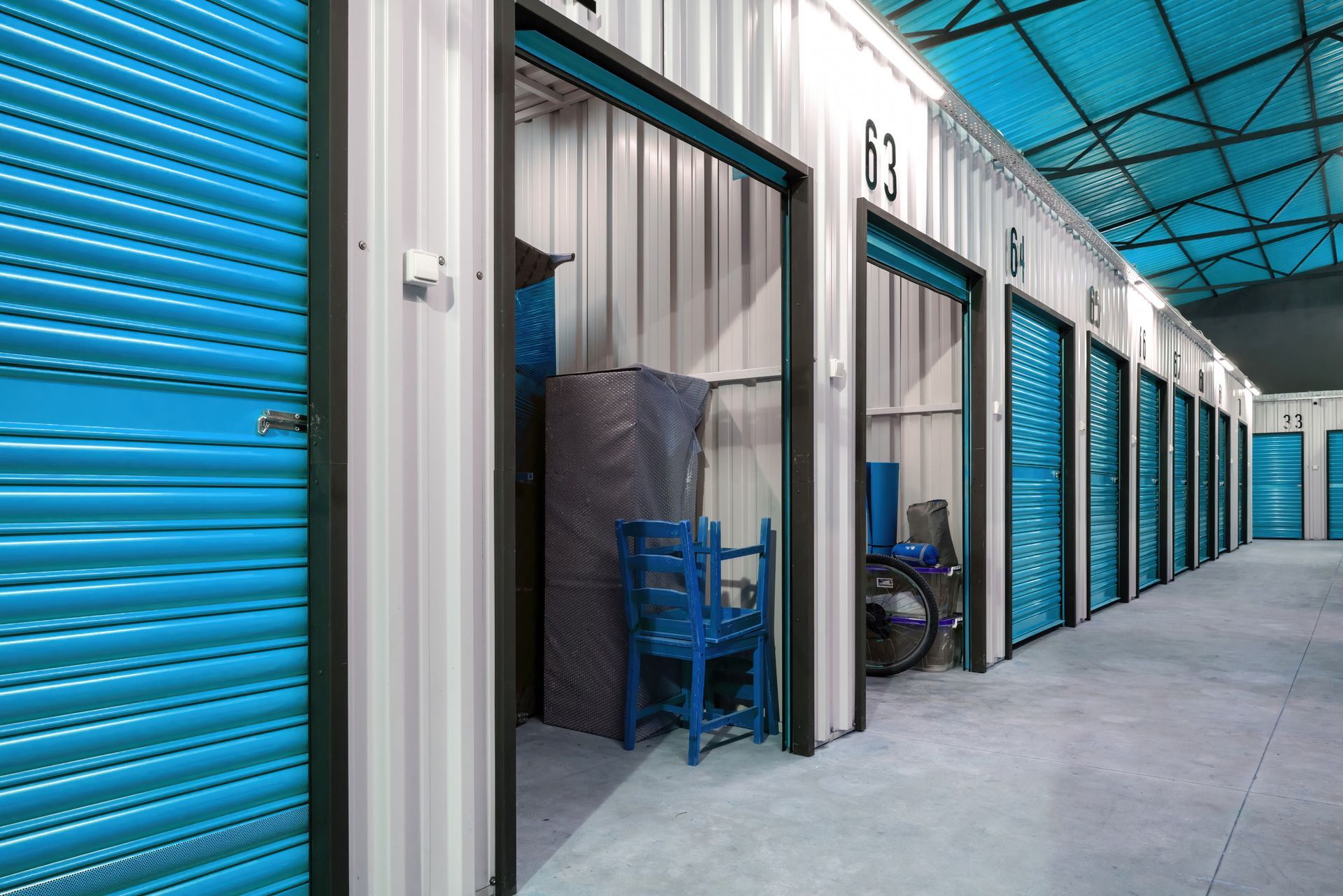 Corridor of silver storage units with blue doors, one of the units with items inside. Corridor of silver storage units with blue doors, one of the units with items inside.