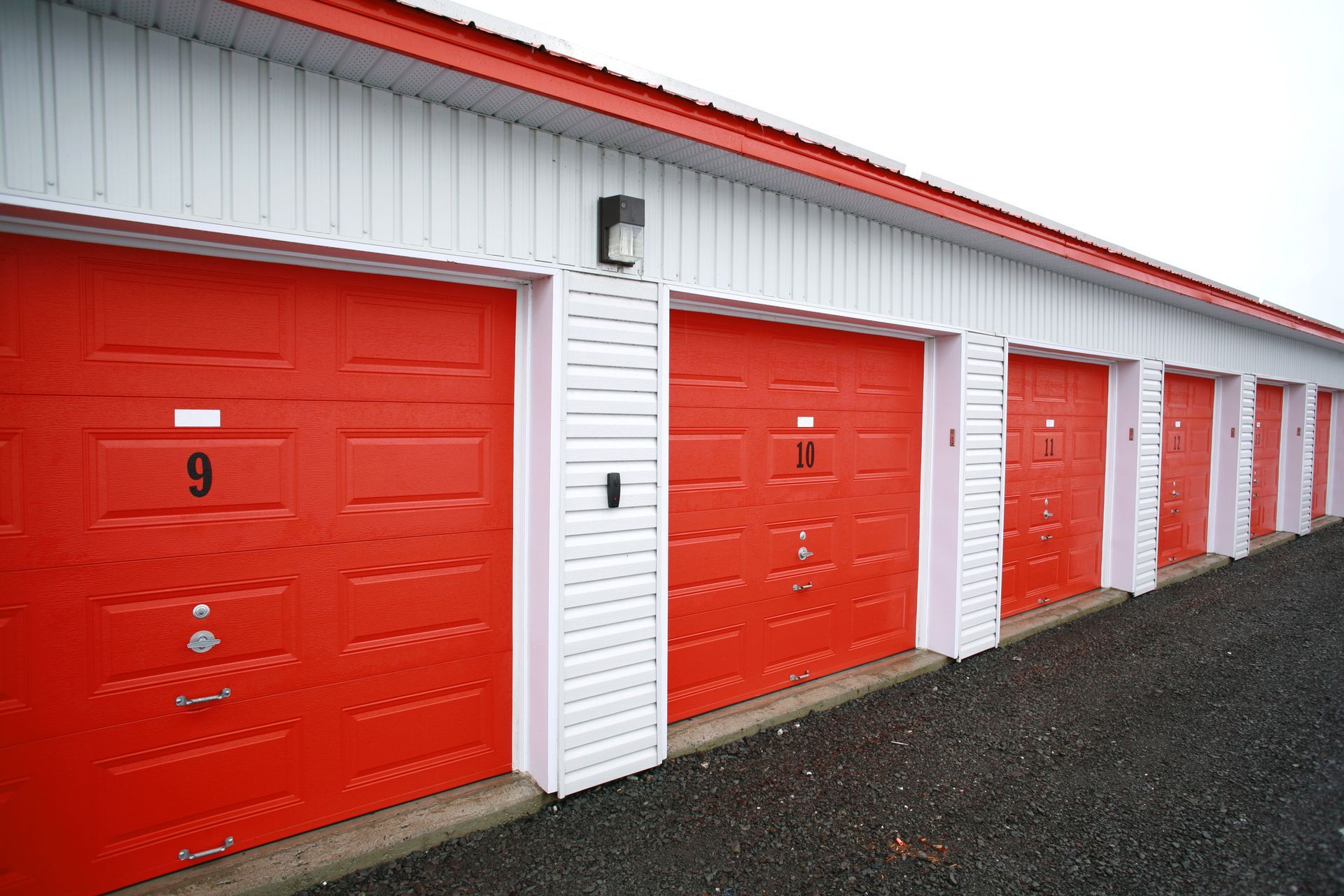 A row of storage units with red sliding doors on a white building.