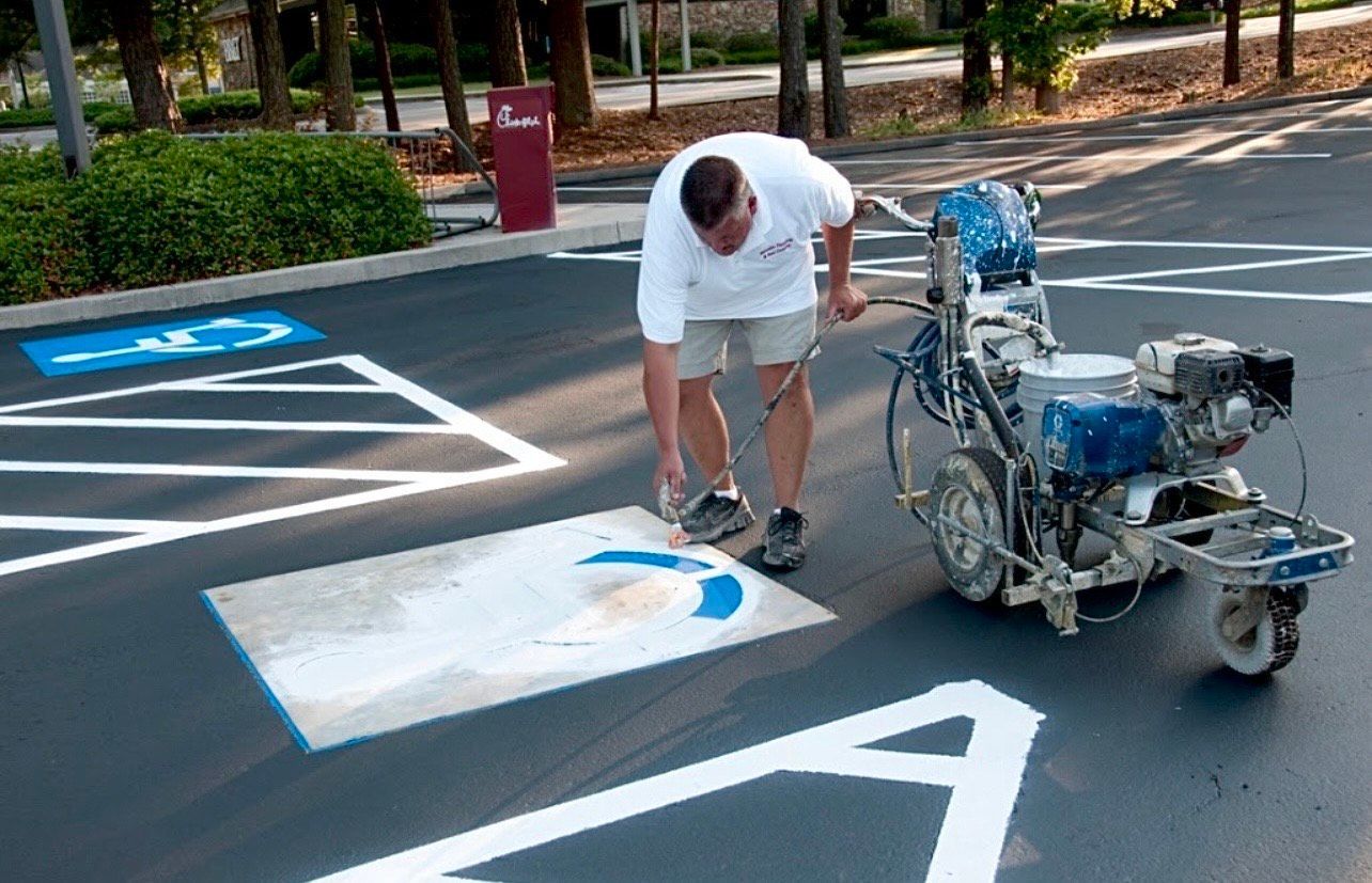 Person painting blue handicap symbol in parking lot with white lines.