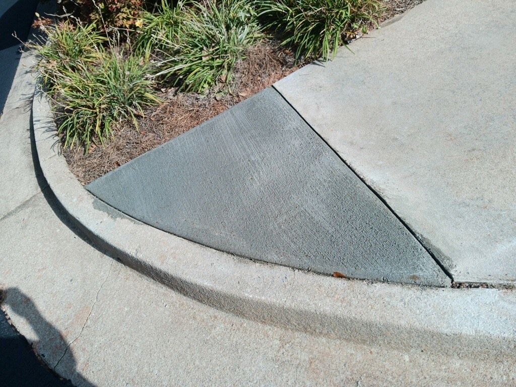 Concrete triangular sidewalk extension at curb, with plants.