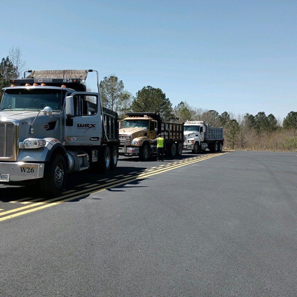 Three dump trucks lined up on a road, ready for work. Blue sky, asphalt, and trees in the background.