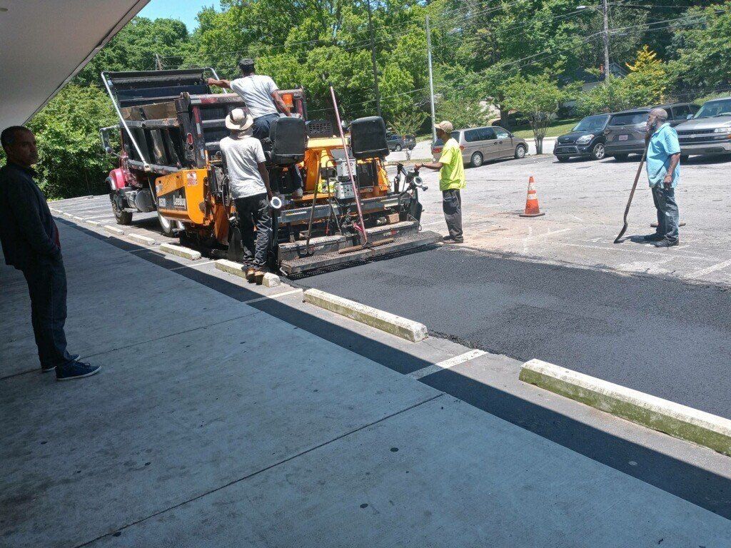 Asphalt paving in progress on a parking lot; workers operate machinery, apply asphalt.