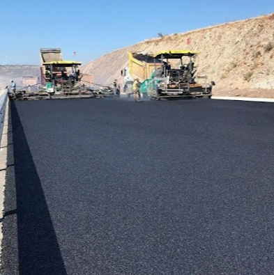 Asphalt paving in progress on a road, with two paving machines and a dump truck.