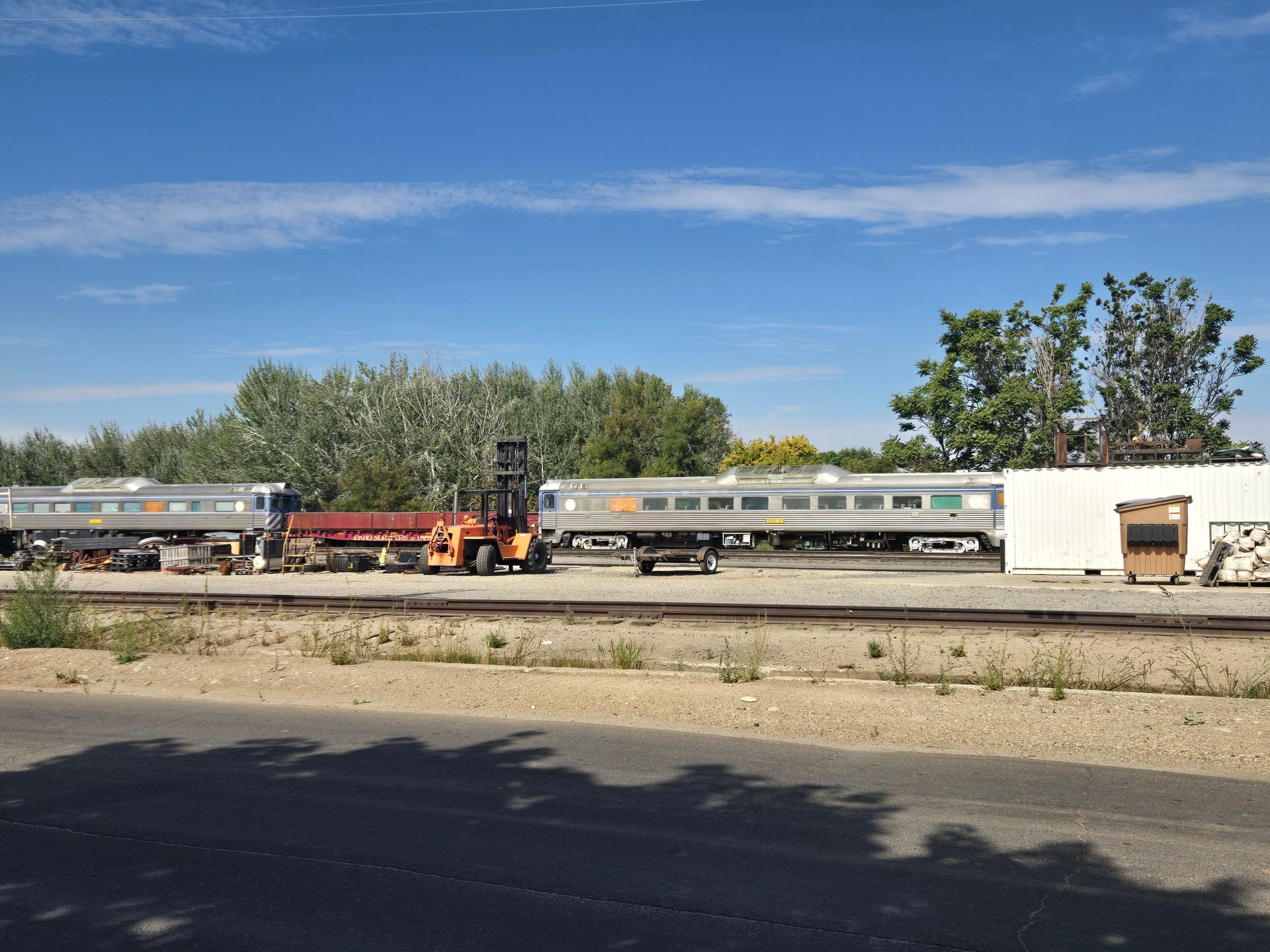 Forklift near train cars on tracks; sunny day.