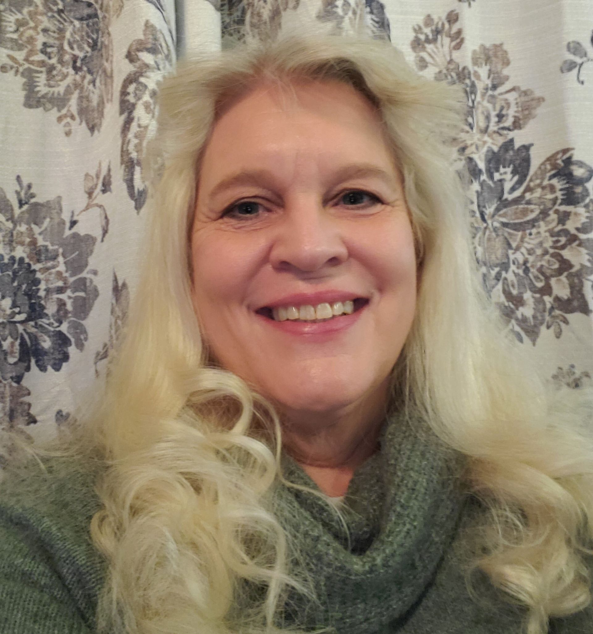 A woman is sitting at a desk with a laptop and a vase of flowers.
