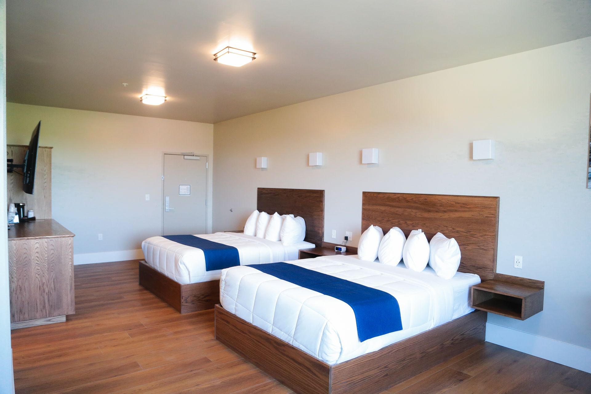 Modern hotel room with two queen beds, white bedding, blue runners, and wood flooring