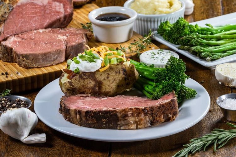 Prime rib dinner with sides of potatoes, broccoli, and asparagus.