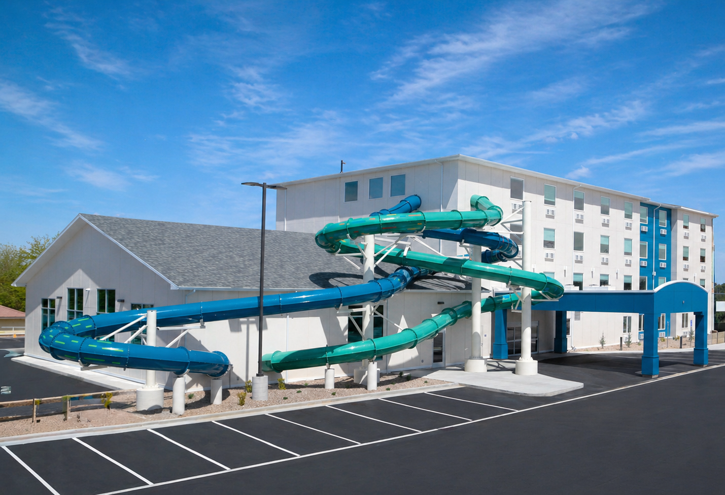 Outdoor water slide structure beside a white hotel building under a bright blue sky