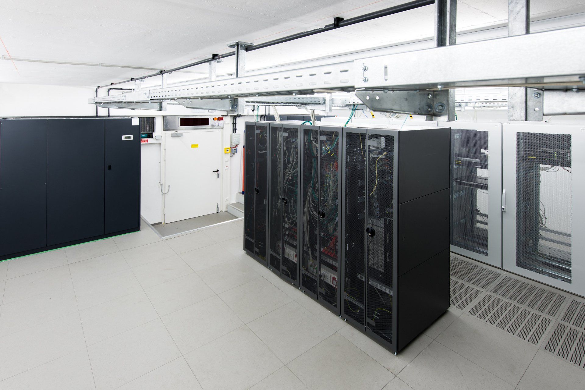 Data center with server racks and equipment; white floors, overhead cables.