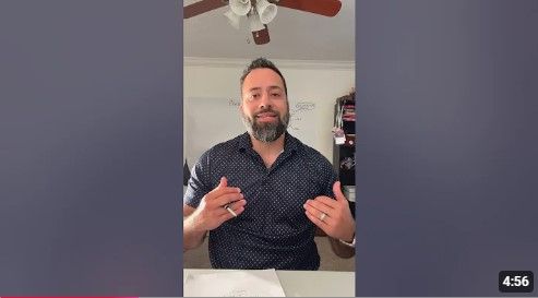 A man with a beard is sitting at a table in front of a ceiling fan.