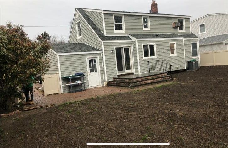 Gray house with white trim and raised deck in a bare backyard