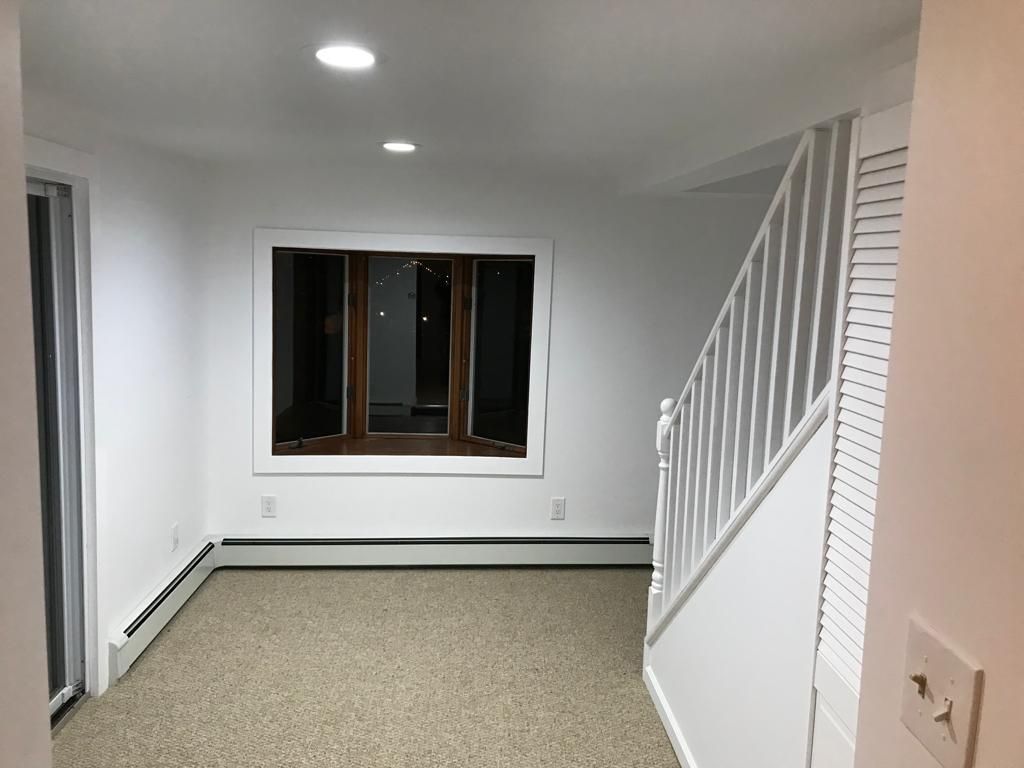 Empty carpeted room with white walls, window, and staircase railing.