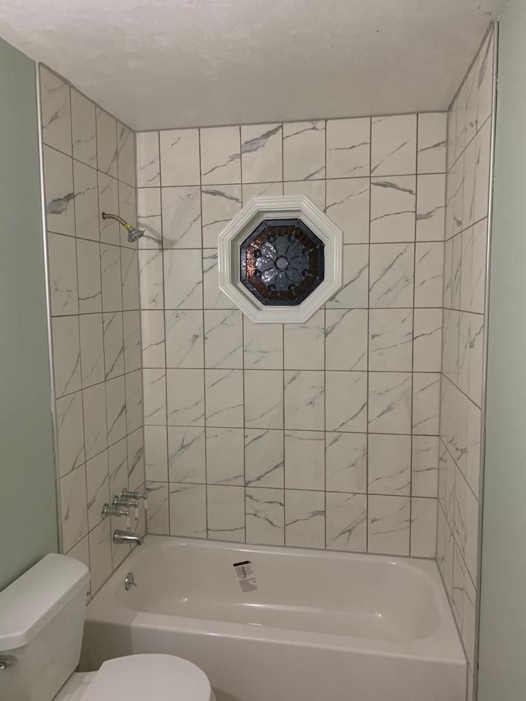 White tiled bathroom with a bathtub and an octagonal window above it.