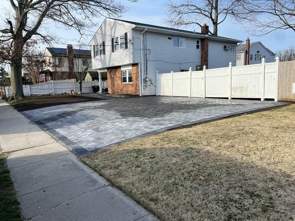Residential house with white fence, paved driveway, and winter lawn along a sidewalk