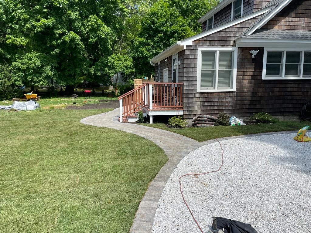 Curved gravel walkway leading to a house with a wooden porch and green lawn in front.