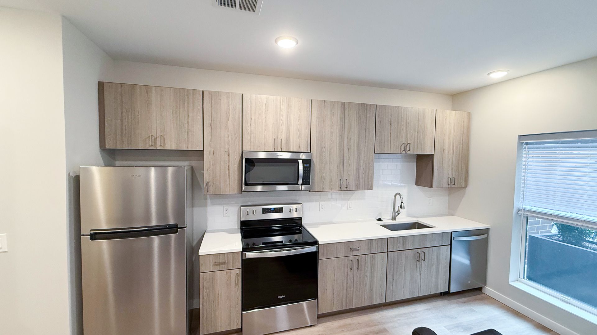 Modern kitchen with stainless steel appliances, light wood cabinets, and a window.
